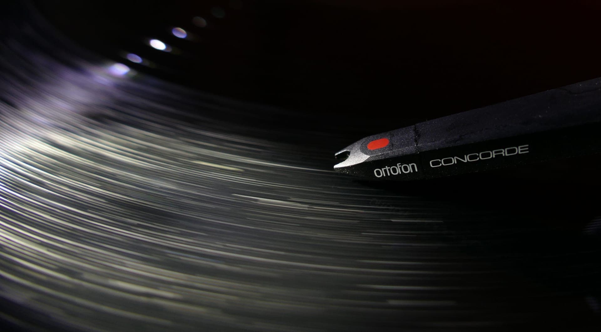 Close-up of a phono cartridge and stylus tracking a record groove